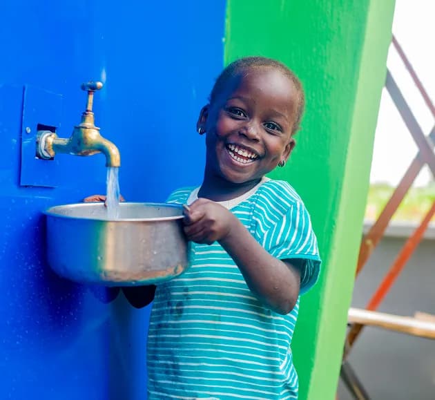 A smiling child filling a bowl with clean water from a tap