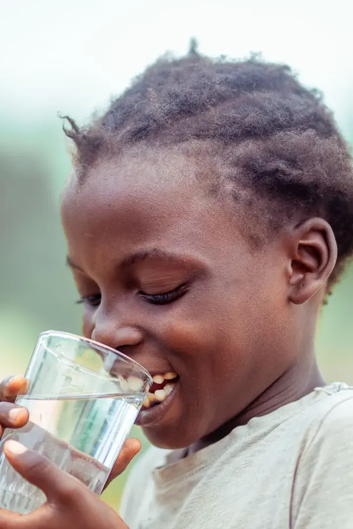 A girl drinking a glass of clean water from a FairAction smart water solution.
