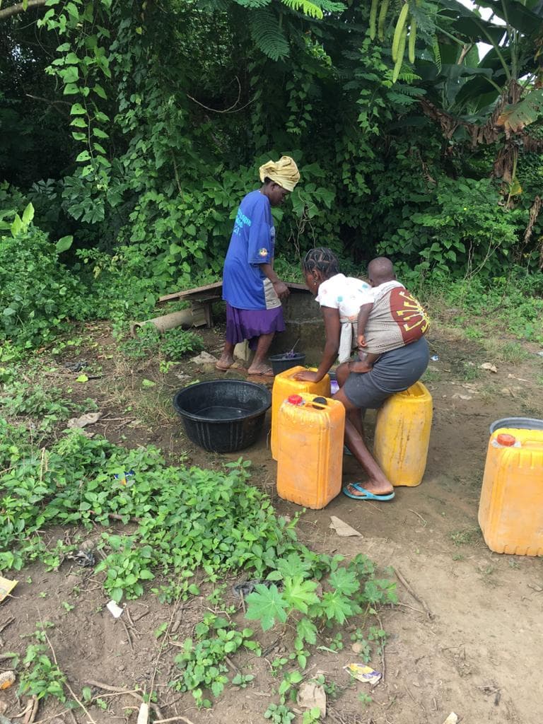 Women filling yellow jerrycans from an unprotected well at Alagba Village, Ibadan, one carrying a baby on her back