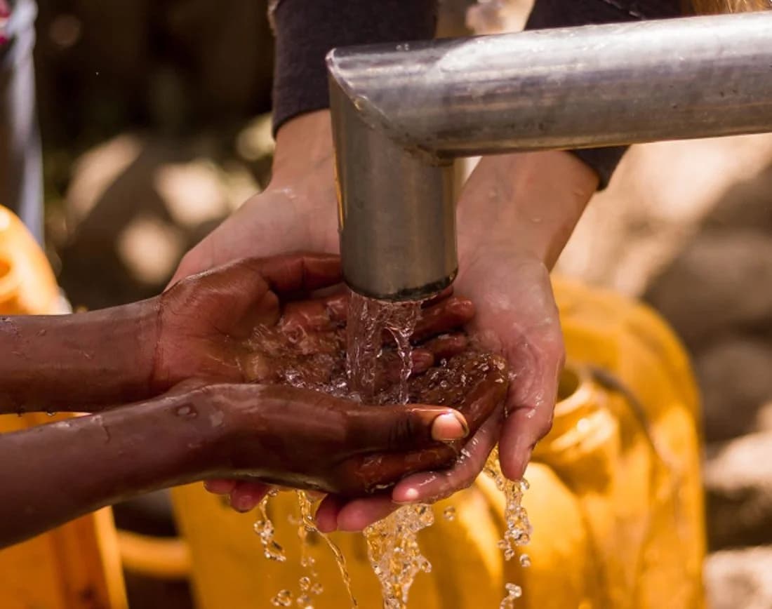 Cupped hands receiving clean running water from a tap.