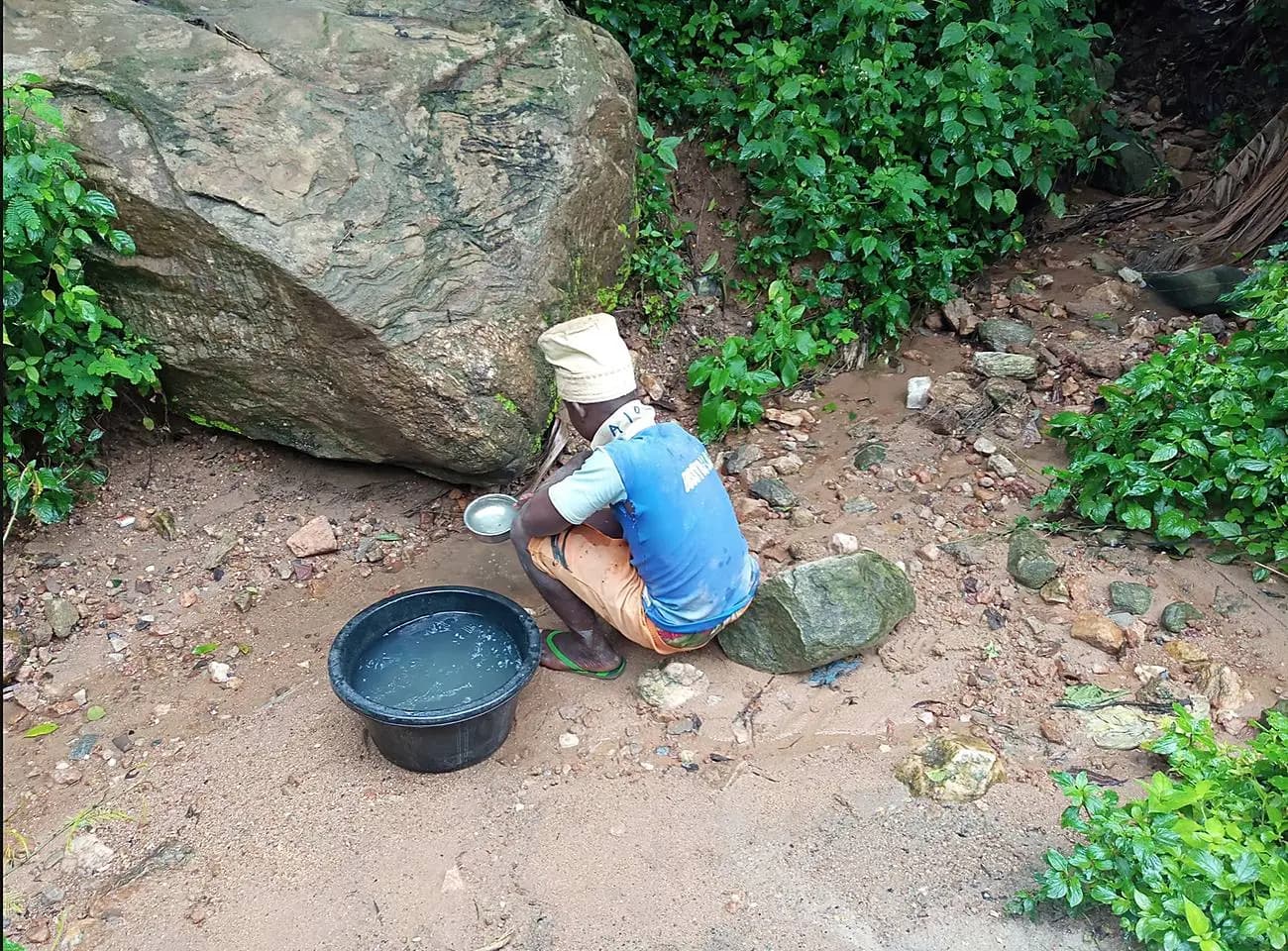 A young boy collecting water by hand from a stream